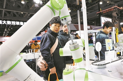 2025上海国际机床展上，参观者在一个进行作业演示的双臂协同机器人前驻足观看。 